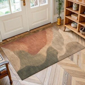 a large rug with a colorful abstract design on a wooden floor. The rug is placed near a set of white doors, and there is a wooden bookshelf in the background.