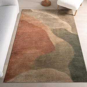 a large, colorful rug with a geometric pattern in shades of brown, green, and orange. The rug is placed on a wooden floor, and there is a white couch and a white chair visible in the background.