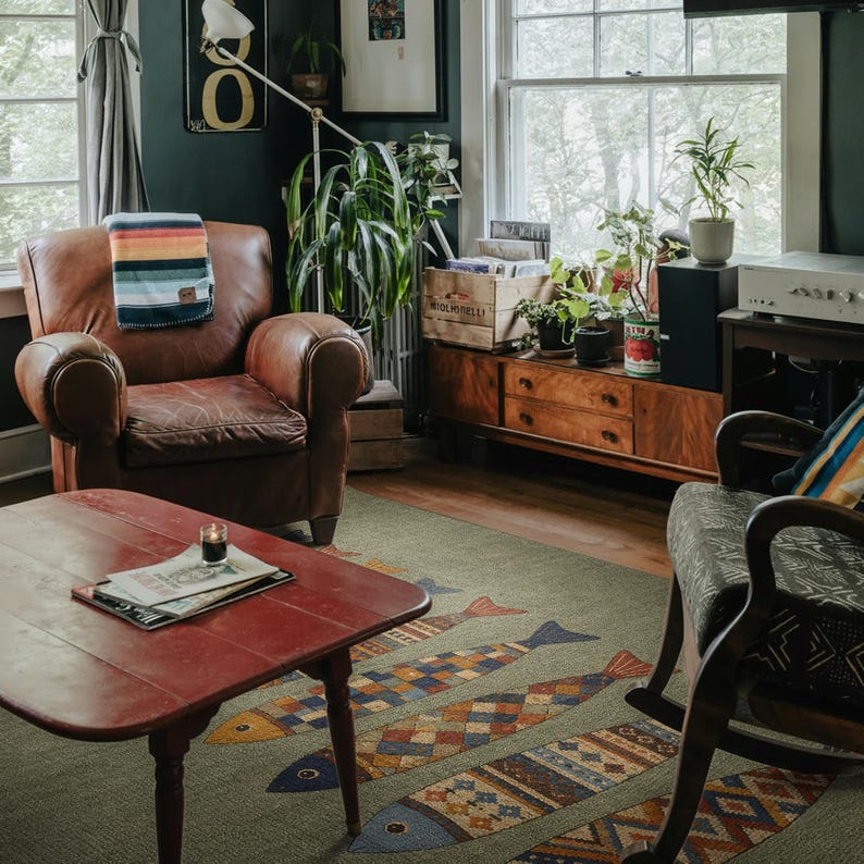 a cozy living room with a brown leather chair, a red coffee table, and a wooden side table with a plant. The room is decorated with various plants, a patterned rug, and a bookshelf.