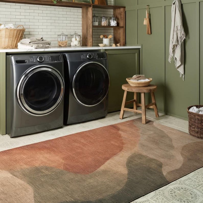 a well-organized laundry room with two washing machines, a wooden stool, and a colorful rug on the floor.