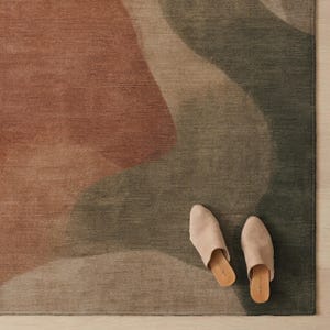 A pair of beige slip-on shoes is placed on a rug with a multicolored abstract pattern.
