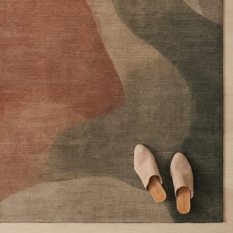 A pair of beige slip-on shoes is placed on a rug with a multicolored abstract pattern.