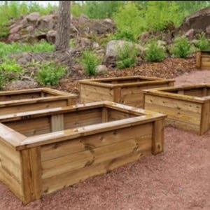 May include: Four rectangular wooden planters with a natural finish are arranged on a reddish-brown surface. The planters have a simple, open design, ideal for gardening. Green foliage and rocks are visible in the background.
