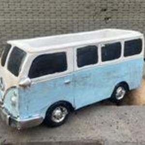 Könnte beinhalten: Ein hellblau-weißer Keramik-Blumentopf in Form eines Oldtimer-VW-Busses. Der Pflanztopf hat schwarze Fenster und verchromte Stoßstangen. Er steht auf einer grauen Oberfläche mit Felsen im Hintergrund. Der Bus ist etwa 20 cm lang.