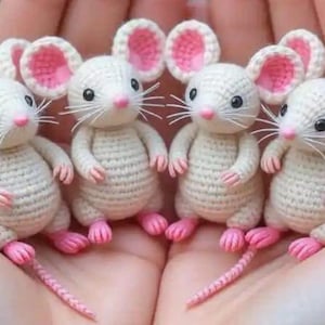 Könnte beinhalten: Vier gehäkelte weiße Mäuse mit rosa Ohren, Pfoten und Nasen. Jede Maus hat schwarze Augen und lange weiße Schnurrhaare. Die Mäuse stehen aufrecht, wobei ihre Schwänze hinter ihnen herziehen. Die Häkelarbeit ist detailliert und strukturiert.