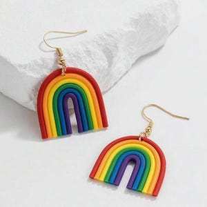 Könnte beinhalten: Ein Paar regenbogenförmige Ohrringe. Jeder Ohrring hat einen roten Bogen mit Schichten aus Orange, Gelb, Grün, Blau und Lila. Die Ohrringe haben goldfarbene Haken.