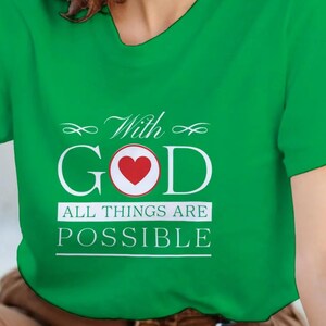 Puede incluir: Camiseta verde con el texto "With GOD" y un corazón rojo en la letra "O". Debajo está escrito "ALL THINGS ARE POSSIBLE" en blanco. La camiseta es de un material suave.