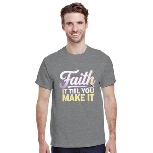 Puede incluir: Una camiseta gris con la frase "Faith IT TIIL YOU MAKE IT" en una fuente multicolor. El texto es blanco, morado y amarillo. La camiseta de manga corta parece estar hecha de un material suave.