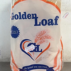 Puede incluir: Una barra de pan en una bolsa de plástico transparente. La bolsa presenta las palabras "Golden Loaf" en azul, con un diseño de espiga de trigo y el texto "the bread you can trust". La fecha de caducidad está impresa en la bolsa.