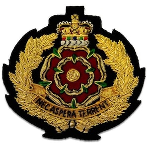 May include: A detailed embroidered emblem featuring a red rose at the center, surrounded by gold-colored wheat stalks and a gold banner with text. The emblem is set against a black background and topped with a gold crown.