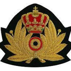 Op de afbeelding: Een zwart en goud geborduurde patch met een rode kroon met gouden accenten, een gouden krans en een rood cirkelvormig embleem. De patch heeft een unieke vorm met puntige randen.