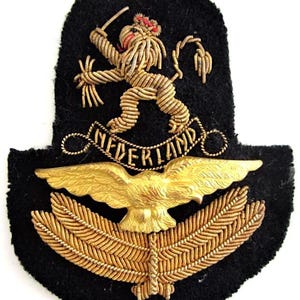 Peut inclure: Écusson militaire néerlandais vintage sur feutre noir. Il présente un lion doré tenant une épée, le mot « NEDERLAND » en or et un aigle doré aux ailes déployées. Le motif est brodé avec du fil doré.