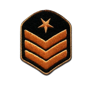 May include: Black and gold embroidered patch featuring a gold star at the top and three gold chevrons below. The patch has a black background and a gold border. This patch is likely a military rank insignia.