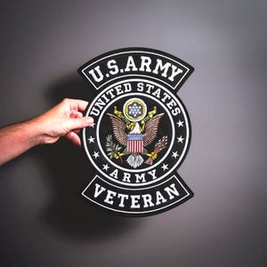 Könnte beinhalten: Ein schwarz-weißer U.S. Army Veteran-Aufnäher mit dem U.S. Army-Emblem mit einem Adler, Sternen und den Worten "U.S. Army", "United States" und "Veteran". Der Aufnäher wird vor einem grauen Hintergrund gehalten.
