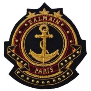 May include: Embroidered patch with a navy blue background, featuring a gold anchor and the words "BALMAIN PARIS" in gold lettering. The patch has a decorative border and is embellished with gold details.