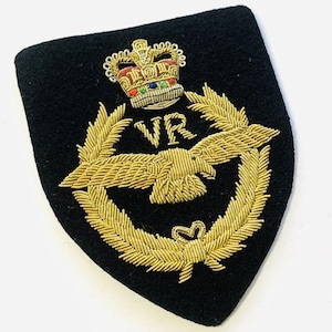 Könnte beinhalten: Ein schwarzer Aufnäher mit goldener Stickerei, die eine Krone, einen Adler und Lorbeerblätter zeigt. Die Buchstaben "VR" sind über dem Adler gestickt. Der Aufnäher hat eine schildförmige Form.