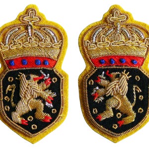 May include: Two embroidered patches with a shield shape, featuring a gold crown, red and blue accents, and a gold lion on a black background. The patches have a yellow border and are likely for decorative purposes.