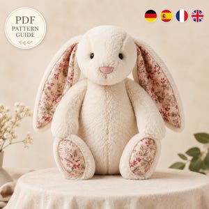 May include: A plush cream-colored rabbit toy with long ears featuring a pink floral pattern on the inner side. The rabbit has a small pink nose and matching floral fabric on the soles of its feet. A circular badge reads PDF PATTERN GUIDE.