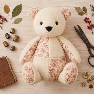 May include: A plush teddy bear constructed from cream-colored fabric and a light pink floral patterned fabric. The bear features dark button eyes and a black stitched nose. It is surrounded by metal thimbles, scissors, buttons, and dried leaves.