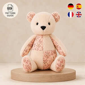 May include: A plush teddy bear constructed from a patchwork of solid cream-colored fabric and a patterned fabric featuring small pink floral and snowflake motifs. The bear has black button eyes, a black stitched nose, and rounded ears.