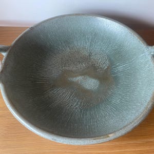 May include: A teal-coloured ceramic serving bowl with two curved handles. The bowl features a textured interior with a radial pattern. The rim and handles are a slightly darker shade of teal.