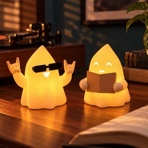 Op de afbeelding: Twee kleine, oplichtende, gebroken witte spookfiguurtjes. Het linker spook draagt een zwarte rechthoekige zonnebril en houdt beide handen omhoog in een rock-gebaar. Het rechter spook heeft een lachend gezicht en houdt een open boek vast.