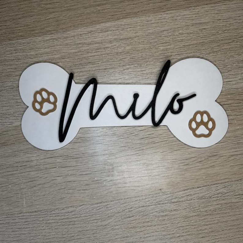 Personalisiertes Hundeschild mit Namen Milo, schwarzem Schriftzug und dekorativen Pfoten.