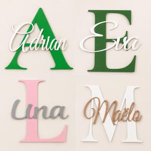 May include: Four large capital letters A, E, L, and M in green, dark green, pink, and white. Each letter features a smaller, cursive-style name layered on top: Adrian in white, Eva in white, Lina in gray, and Ma&euml;lo in a light brown wood tone.