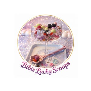 Könnte beinhalten: Ein klares Weinglas gefüllt mit bunten Perlen, künstlichen Beeren und Eiswürfeln steht auf einem Tablett. Ein rosa Löffel mit Beeren liegt neben dem Glas. Das Bild hat den Text "Bibis Lucky Scoops".