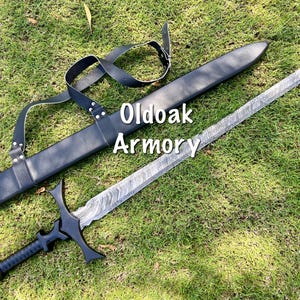 May include: A sword with a patterned blade and black handle, lying on green grass next to a black sheath. The sword has a crossguard and a rounded pommel. The text "Oldoak Armory" is visible.