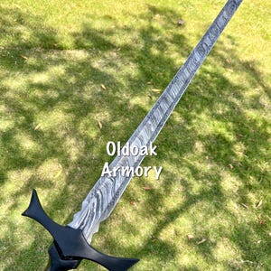 May include: A long, ornate sword with a patterned blade and a black handle and crossguard. The text "Oldoak Armory" is visible on the blade. The sword is held against a backdrop of green grass.