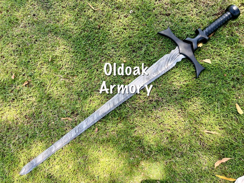 May include: A long, silver and black sword with a textured blade and a black handle. The sword has a crossguard and a rounded pommel. The text "Oldoak Armory" is visible on the image.