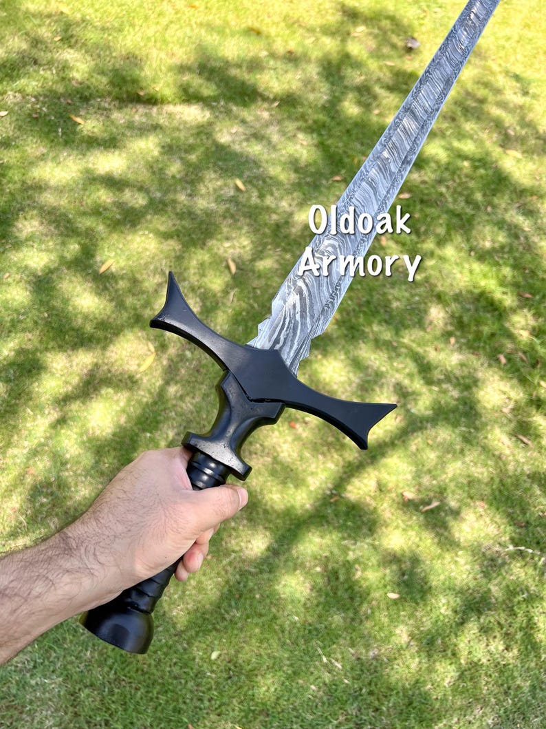 May include: A black sword with a patterned blade is held against a green grassy background. The sword has a black handle and crossguard. The text "Oldoak Armory" is visible on the blade.