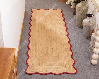 Puede incluir: Una alfombra rectangular de yute con un borde rojo festoneado. La alfombra tiene un color beige natural y una textura tejida. La alfombra mide aproximadamente 152 cm de largo y 76 cm de ancho, adecuada para un pasillo o entrada.