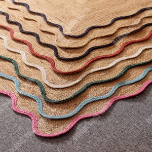 Puede incluir: Primer plano de una alfombra de yute natural con un dise&ntilde;o de borde festoneado. La alfombra presenta una serie de bordes ondulados en varios colores, incluyendo rosa, azul, verde, blanco, rojo y marino. La alfombra est&aacute; hecha de un material tejido.