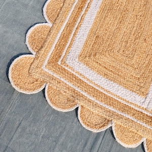 May include: A close-up of a natural jute rug with a scalloped edge. The rug features a woven design with a light tan color and white stripes. The rug is placed on a blue surface.
