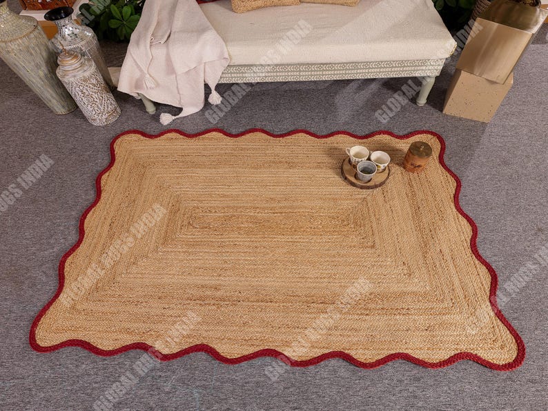 Puede incluir: Una alfombra rectangular de yute con un borde rojo festoneado. La alfombra tiene un color beige natural y una textura tejida. Peque&ntilde;as tazas y un posavasos de madera est&aacute;n sobre la alfombra. Esta alfombra es adecuada para salones y dormitorios.