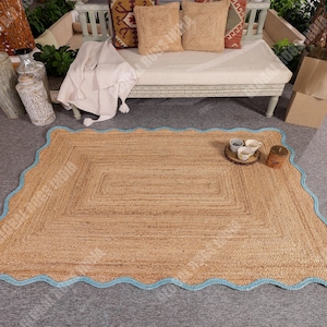 Puede incluir: Una alfombra rectangular de yute de color marr&oacute;n claro con un borde festoneado azul claro. La alfombra tiene una textura tejida y est&aacute; colocada sobre una superficie gris. Hay objetos decorativos alrededor de la alfombra.