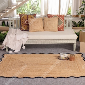Puede incluir: Una alfombra rectangular de yute con un borde negro festoneado. La alfombra es de color marr&oacute;n claro con un dise&ntilde;o tejido. Cojines decorativos en tonos beige, naranja y marr&oacute;n est&aacute;n sobre un banco blanco. Una manta blanca con borlas est&aacute; sobre el banco.