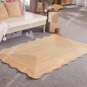Puede incluir: Una alfombra rectangular de yute con borde festoneado. La alfombra es de color beige natural y tiene una textura tejida. Se coloca sobre un suelo alfombrado gris. La alfombra es un revestimiento de suelo decorativo.