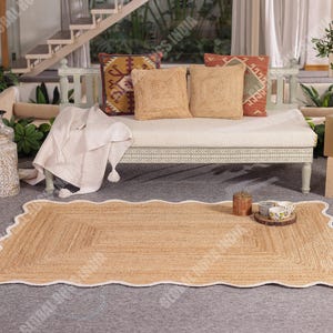 Puede incluir: Una alfombra rectangular de yute con un borde blanco festoneado. La alfombra est&aacute; colocada sobre una superficie gris frente a un banco blanco con cojines decorativos. Tambi&eacute;n se ven jarrones decorativos y una bandeja de madera con cuencos peque&ntilde;os.