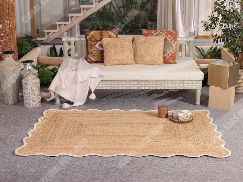Puede incluir: Una alfombra rectangular de yute con un borde blanco festoneado. La alfombra est&aacute; colocada sobre una superficie gris frente a un banco blanco con cojines decorativos. Tambi&eacute;n se ven jarrones decorativos y una bandeja de madera con cuencos peque&ntilde;os.
