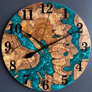 May include: Round wooden wall clock with a natural wood grain pattern and teal epoxy resin accents. The clock features black numerals and hands, creating a striking contrast. A unique, handcrafted home decor item.