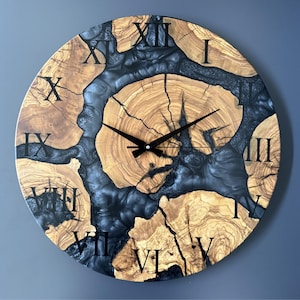 May include: A round wooden wall clock with a natural wood grain pattern and black Roman numerals. The clock face features a dark blue resin filling the gaps in the wood. The clock hands are black.