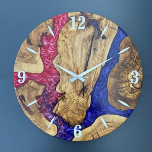 May include: A round wooden wall clock with a natural wood grain center and a red and blue epoxy resin design. The clock features white numerals at the 12, 3, 6, and 9 positions, with white hands. The clock's diameter is approximately 18 inches.