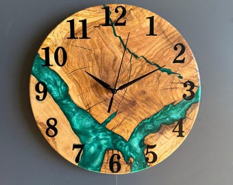 May include: A round wall clock made from a natural wood slice with a prominent, swirling emerald green resin inlay. The clock face features black Arabic numerals from 1 to 12 and thin black metal hour, minute, and second hands.