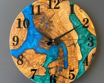 May include: Round wooden wall clock with a natural wood grain pattern. The clock face features blue and teal resin accents, black numerals, and black clock hands. The clock measures approximately 12 inches in diameter.