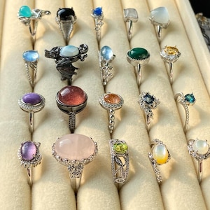 May include: A collection of silver rings with various gemstones, including turquoise, black onyx, blue sapphire, moonstone, emerald, and amethyst. The rings feature diverse designs, from simple bands to ornate settings with intricate details. The gemstones are oval, round, and pear-shaped.