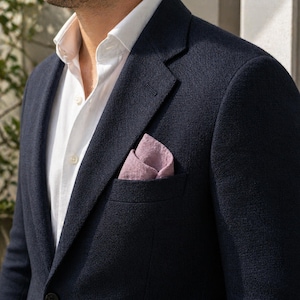Dusty pink organic muslin handkerchief used as a stylish pocket square in a men's navy blue blazer. Rustic wedding groomsmen accessory, textured cotton hankie for men, sustainable suit styling, casual boho groom pocket square.