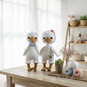 Amigurumi crochet goose plush couple on a rustic wooden table with delicate baby's breath flowers, a small succulent, and yarn. A charming scene for a baby shower gift or nursery decor.